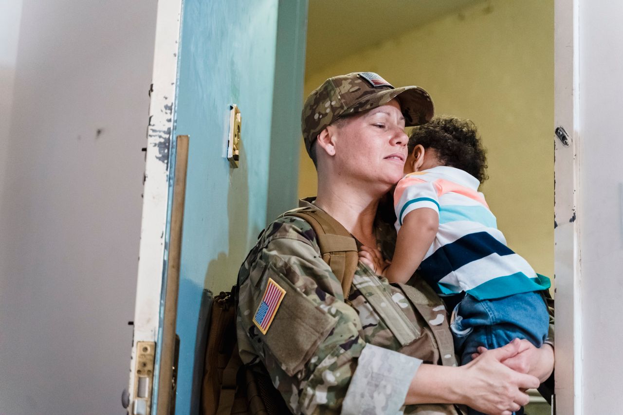 Soldier mother embraces her child at the doorway, a heartfelt family moment.