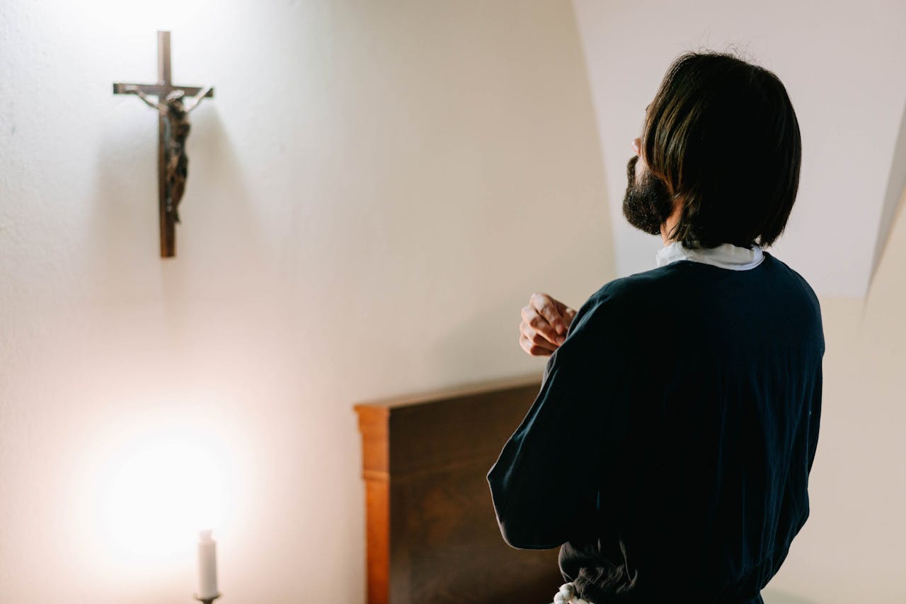A man in prayerful reflection before a crucifix in a serene, dimly lit room