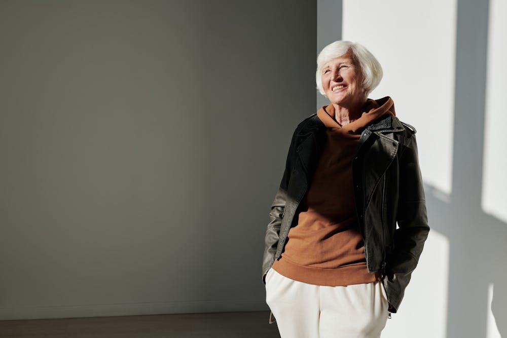 Senior woman exudes confidence in trendy leather jacket indoors with sunlight