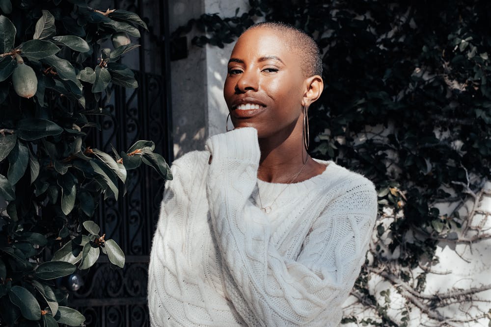 A smiling young woman in a white sweater enjoying the sunlight outdoors among green leaves