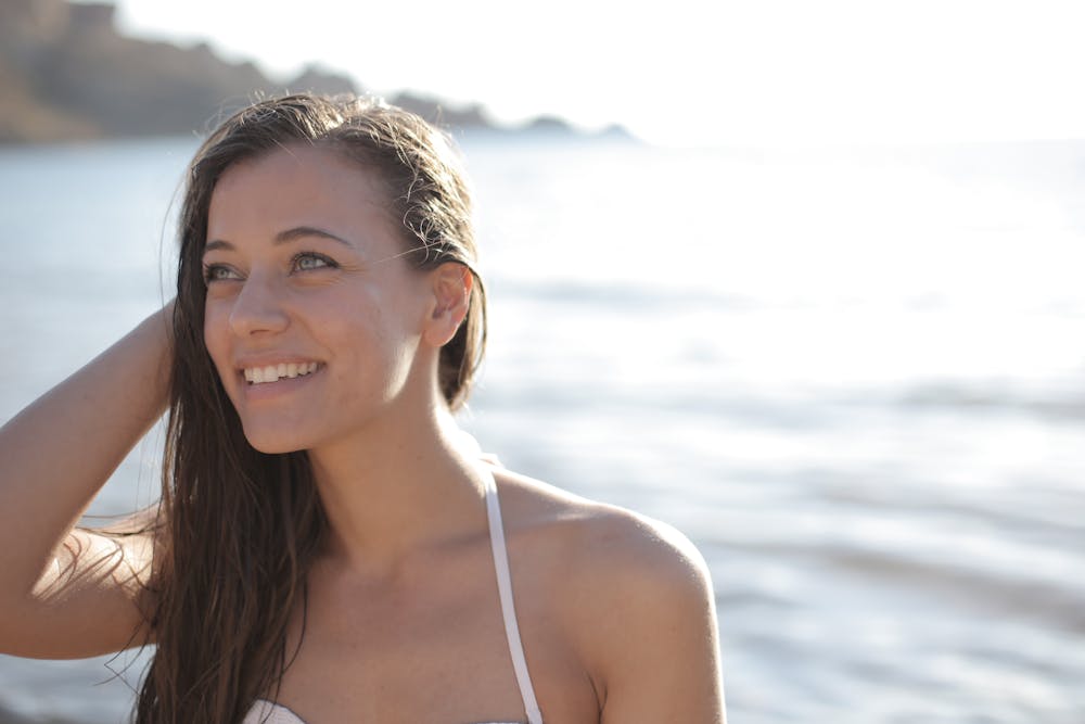 A woman with a bright smile enjoys a sunny day by the ocean, conveying happiness and relaxation.
