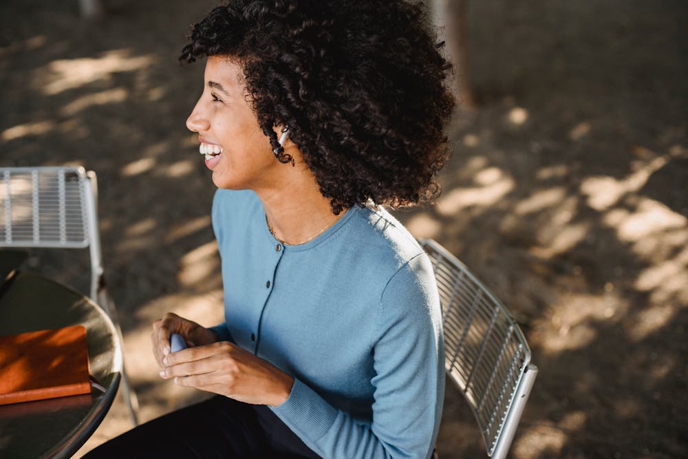 A cheerful woman listens to music on wireless earphones while enjoying a sunny day in the park