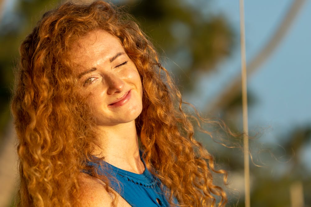 A cheerful woman with curly hair winking and smiling in sunlight.