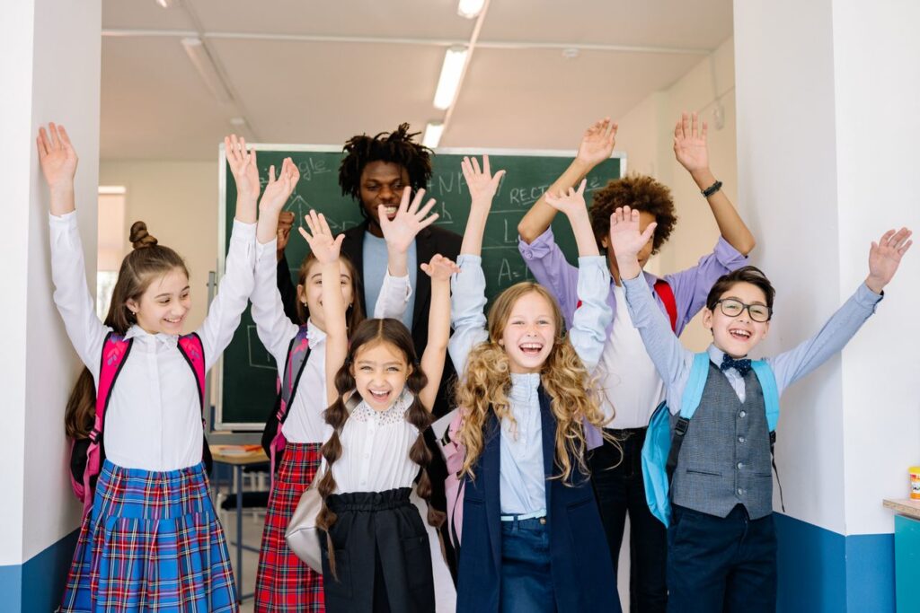 Joyful group of diverse school children raising their hands in an indoor classroom setting
