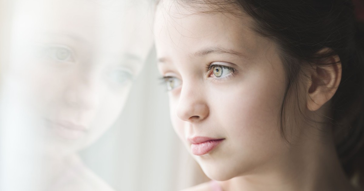 Crop calm young girl with bright expressive eyes and brown hair leaning against window looking out