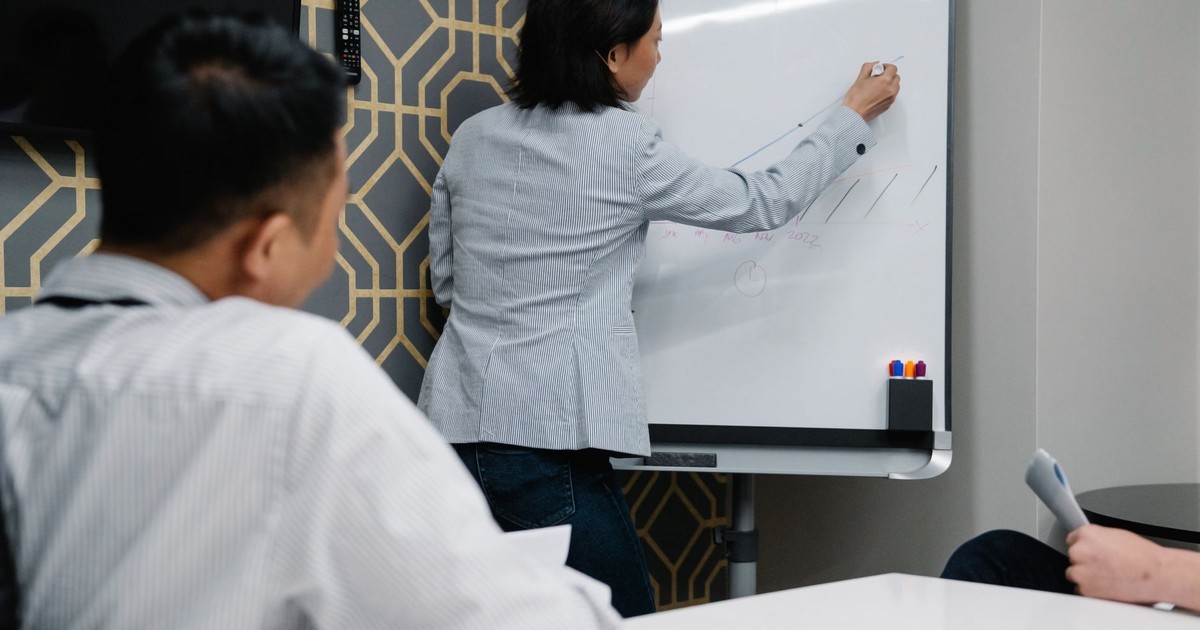 Businesswoman presenting on whiteboard during a team meeting inside a modern office.