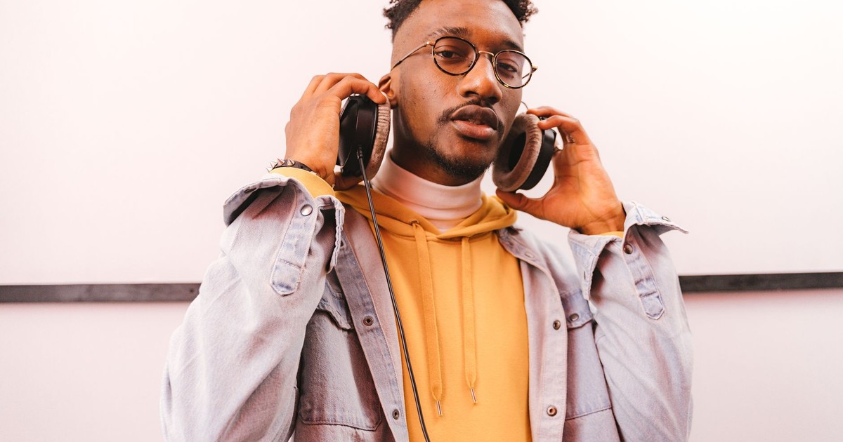 Young man in a denim jacket enjoying music with headphones indoors.