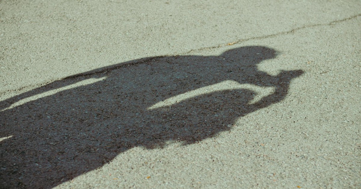 Shadow of a person holding a camera reflected on a pavement surface.