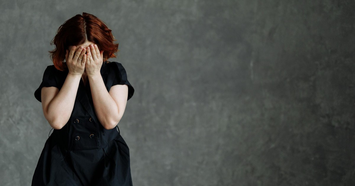A woman in a black dress expressing emotion against a concrete backdrop, highlighting themes of sadness and stress.