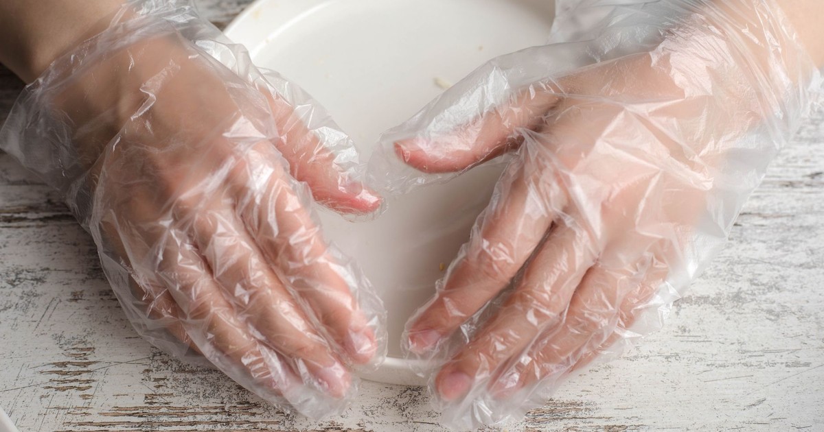 Close-up of hands in plastic gloves holding a plate on a wooden surface.