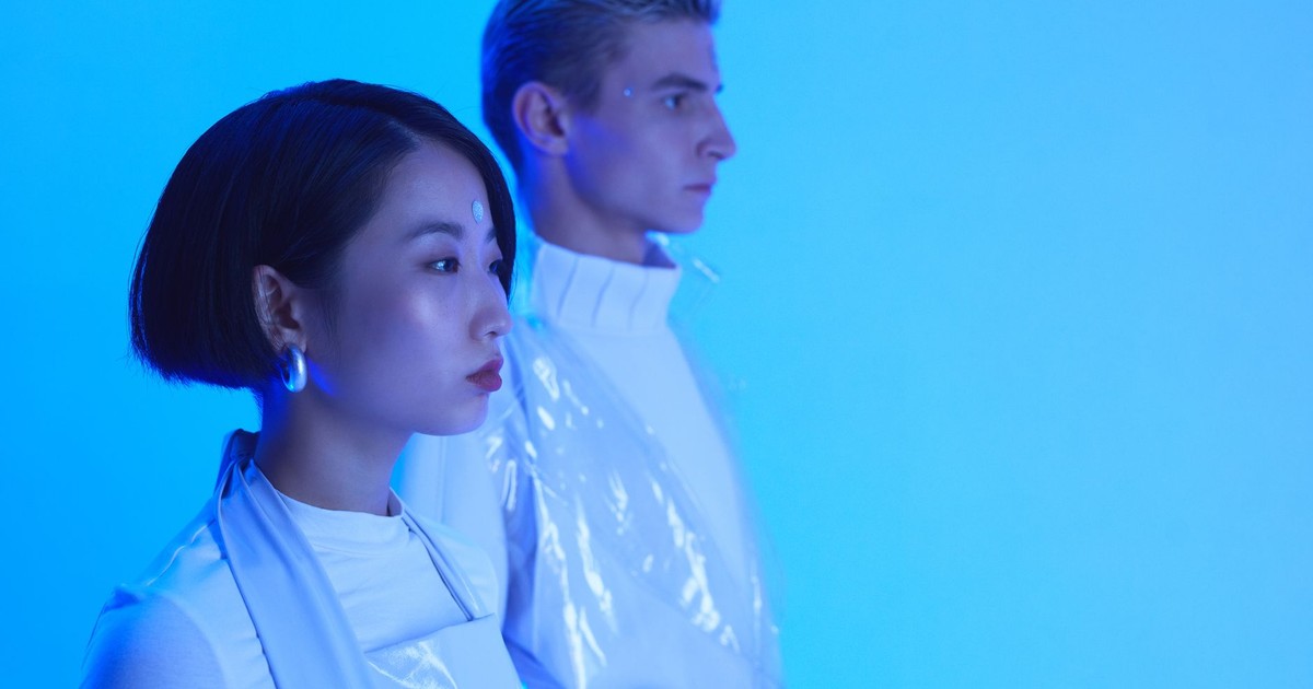 Futuristic fashion portrait of an Asian woman and Caucasian man in blue lighting, showcasing minimalist style.