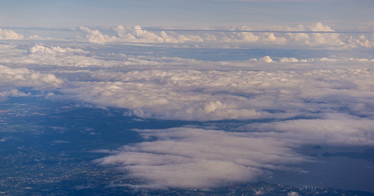 Captivating aerial view of fluffy clouds hovering over a landscape and water body during the day.