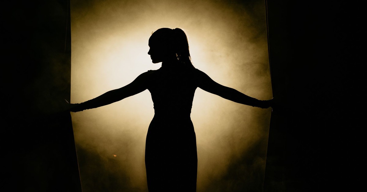 Artistic silhouette of a woman opening stage curtains, surrounded by smoke and spotlight.