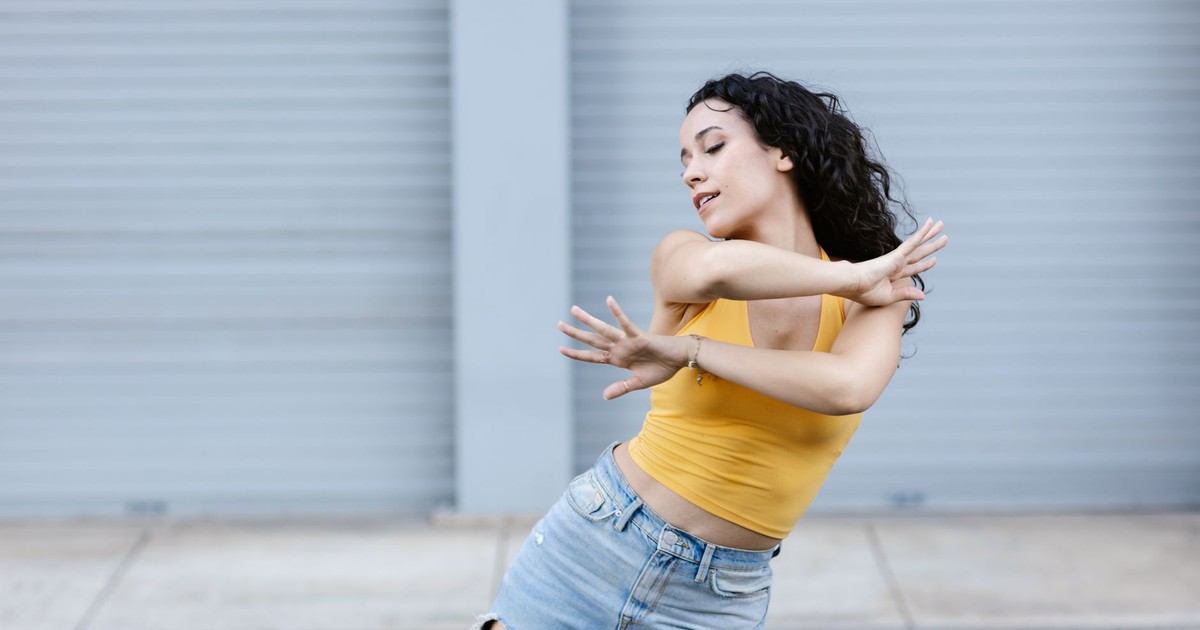 Energetic street dancer in a yellow top and ripped jeans performing outdoors.
