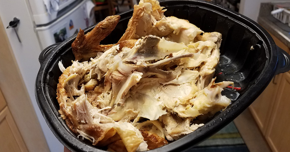 hand holding leftover chicken in black plastic container in kitchen