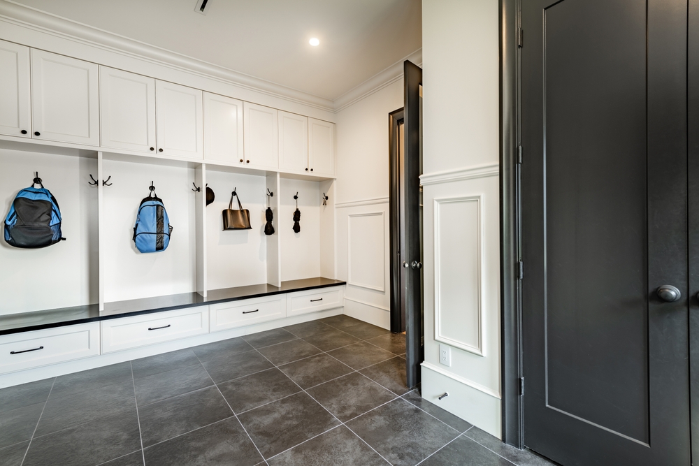 Interior mud room cloak room closet entry way space for hanging coats and backpacks bags umbrellas kids shoes storage area slate flooring black cabinets and floor to ceiling cupboards houseplant 