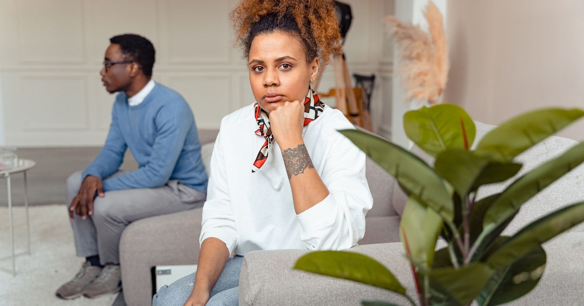 A man and woman sitting apart in a stylish living room, looking contemplative.