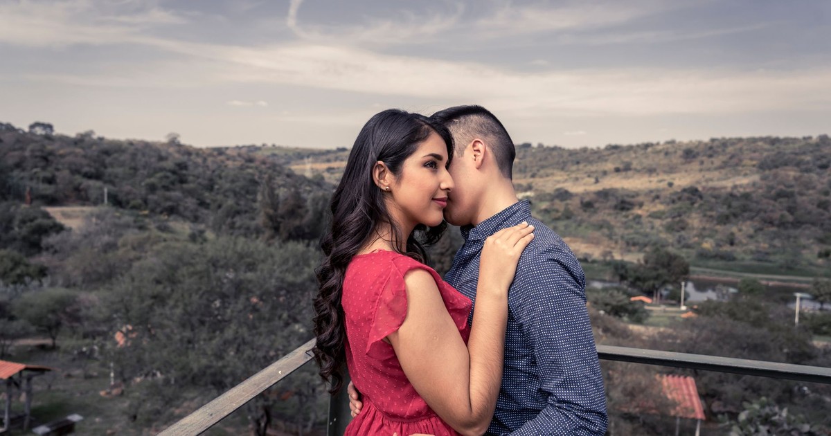 A couple lovingly embracing on a terrace with a scenic landscape in the background.
