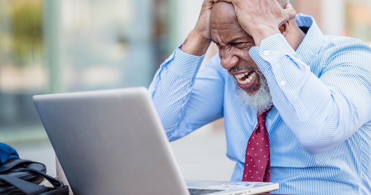 African American man showing frustration with laptop outdoors.