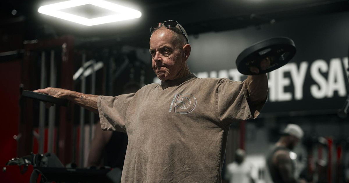 A senior man performs weightlifting exercises inside a dimly lit gym.