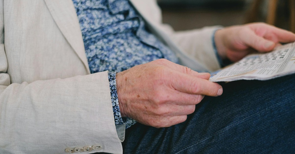 Close-up of a senior adult's hand holding a newspaper in a calm setting.