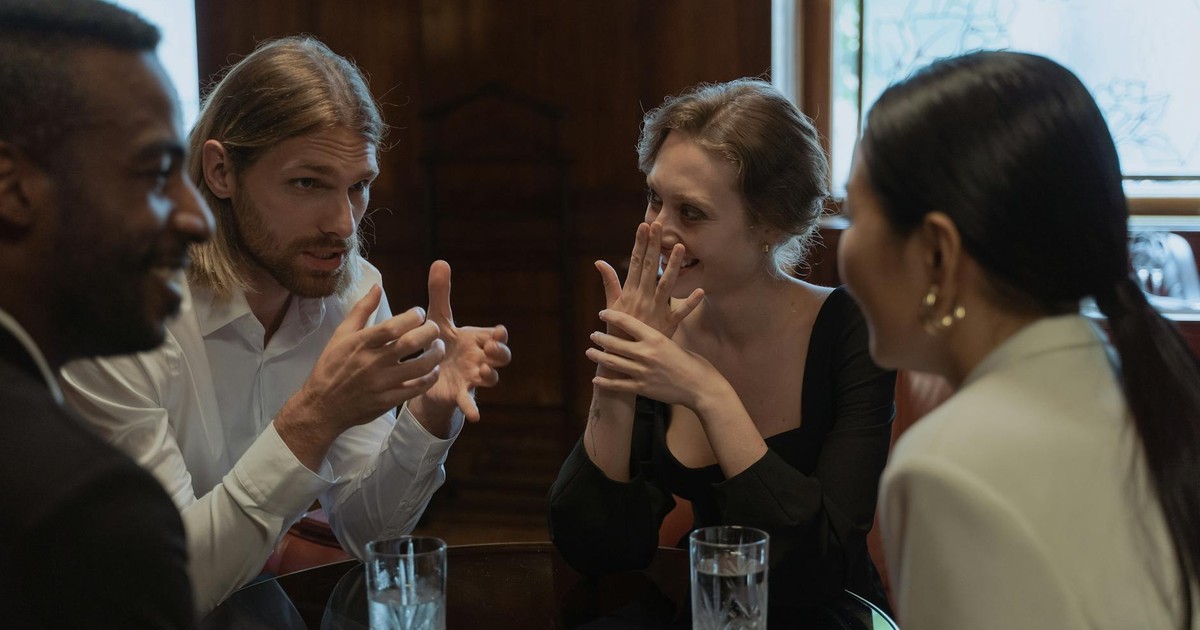 A group of friends talking and laughing around a table in a cozy indoor setting.