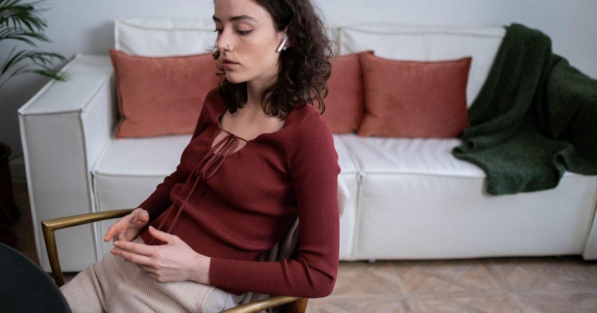 A young woman with curly hair enjoys music through wireless earphones while sitting at home.