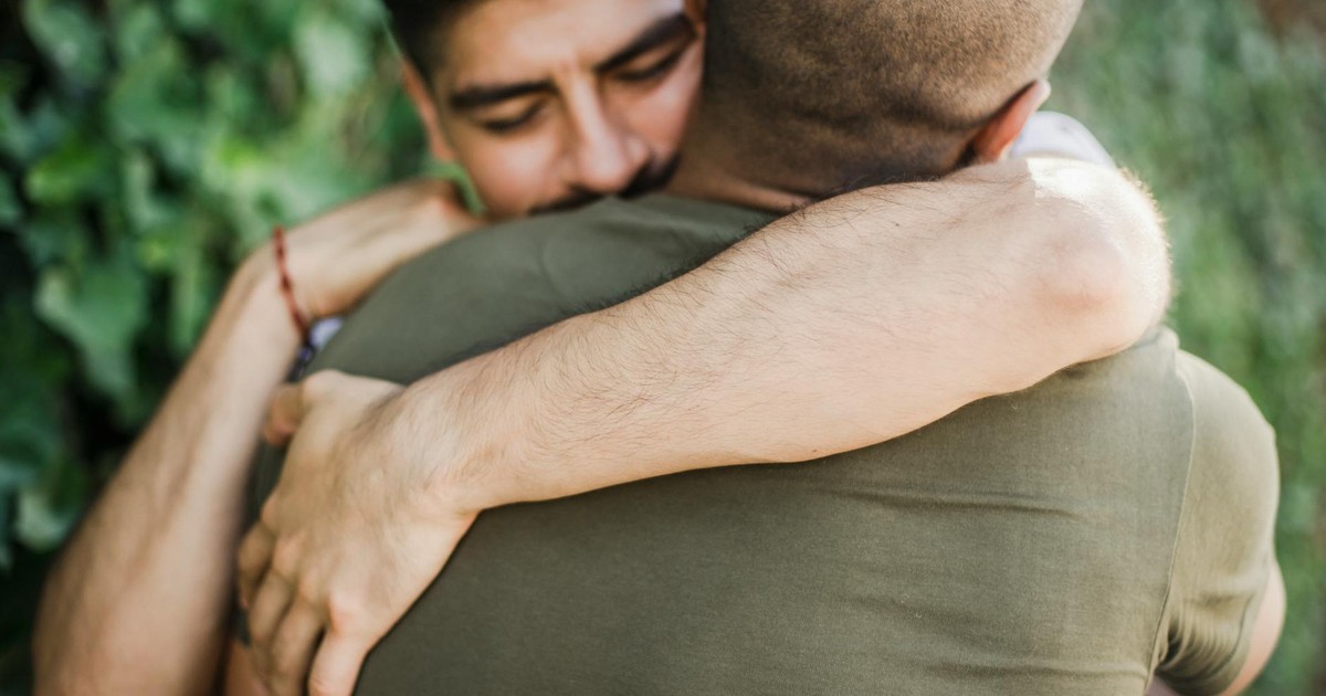 Intimate moment between two men sharing a warm hug outdoors, captured in natural light.