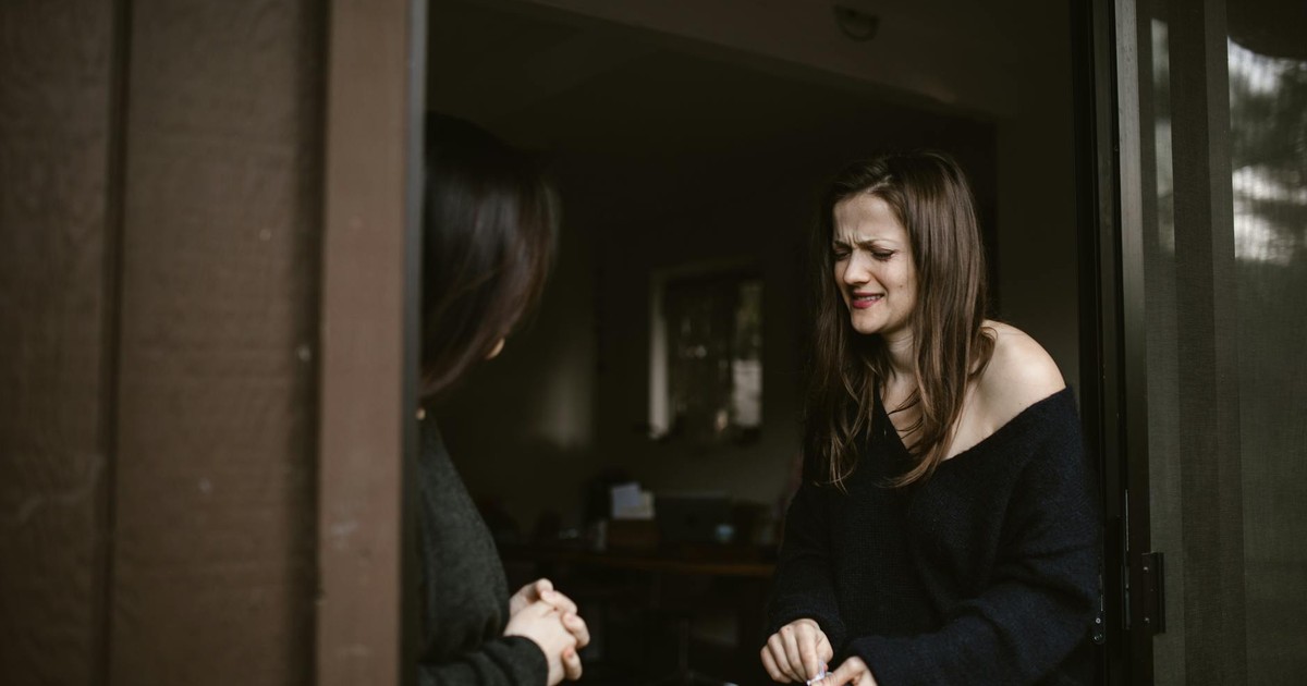 A woman expressing emotions at a doorway, another person partially visible.