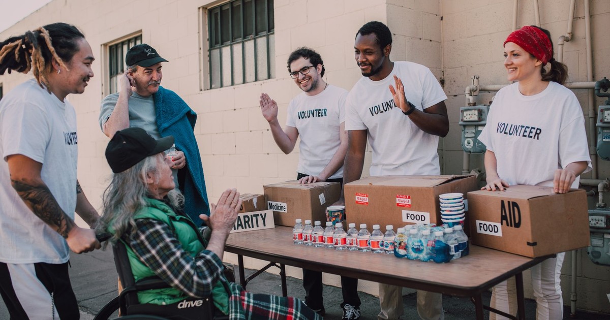 Group of volunteers providing food and aid to a person in wheelchair outdoors.