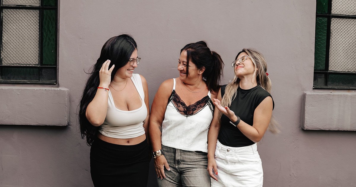 Three adult women smiling and interacting casually against an outdoor wall in Argentina.