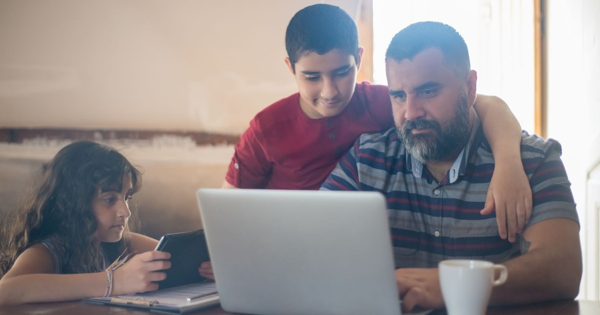 Father and kids using a laptop and tablet at home, enjoying family time together.