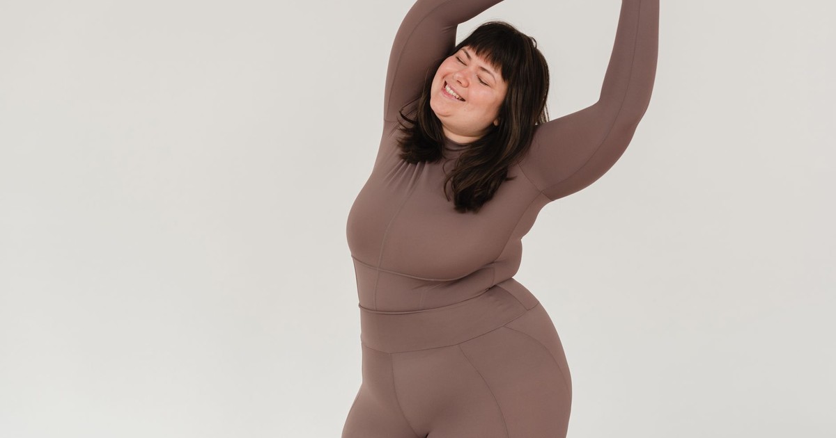Positive plus size female in sportswear stretching oneself with closed eyes against white background