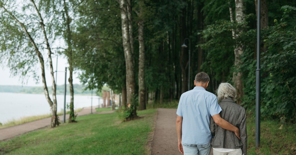 Senior couple strolls arm-in-arm on a tranquil forest pathway, embodying love and togetherness.