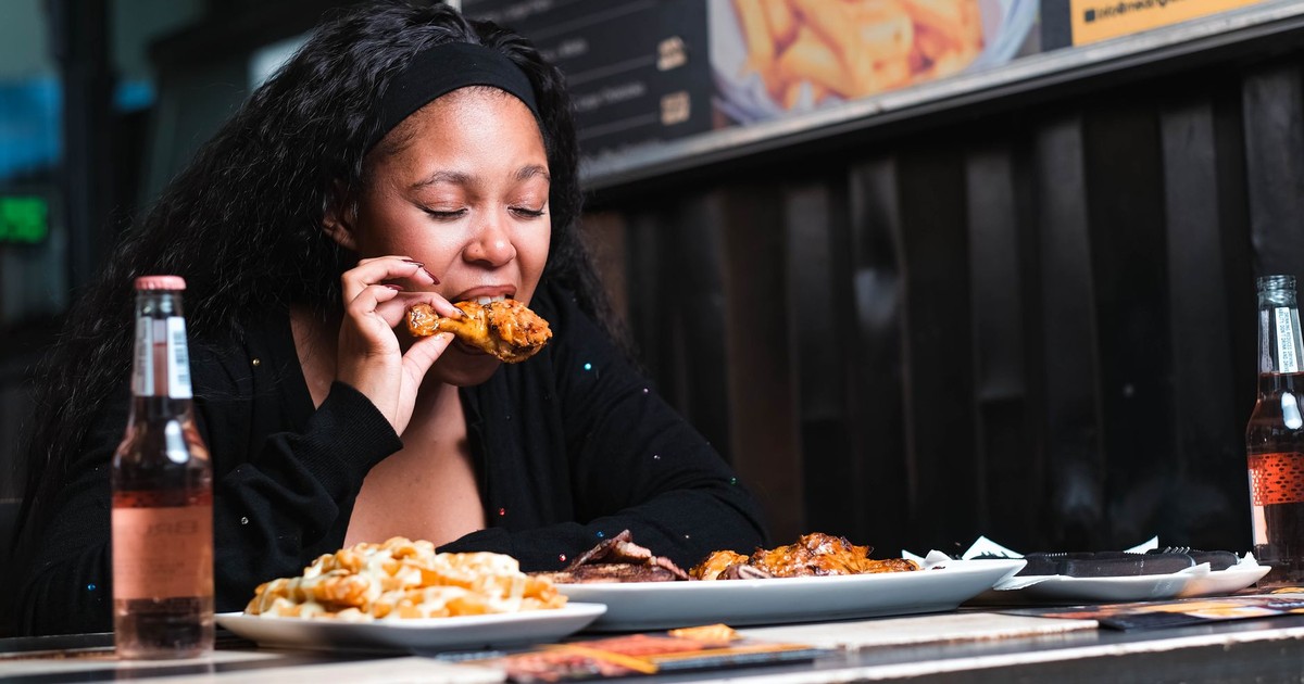 A young woman enjoying a chicken meal at a restaurant, accompanied by drinks and fries.