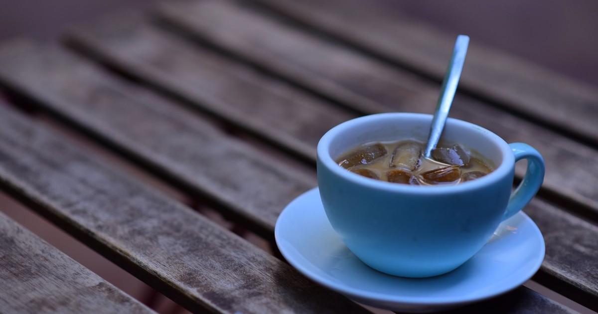 A refreshing iced coffee served in a blue cup on a rustic wooden table, perfect for summer outdoor vibes.