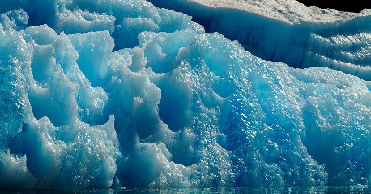 A stunning view of a blue iceberg with intricate textures, floating in the calm ocean.