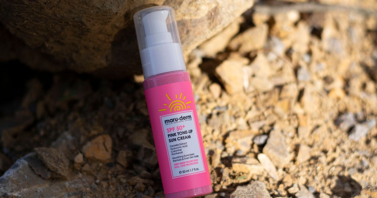 Close-up of SPF 50+ sun cream bottle with pink toned packaging on rocky surface.