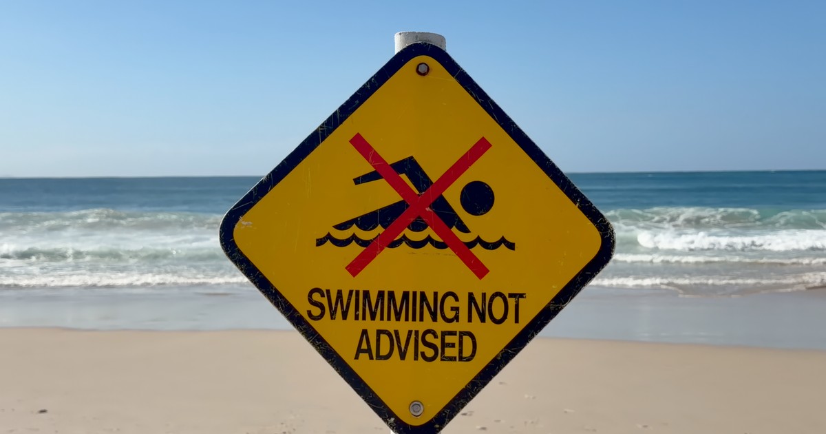 Warning sign on Byron Bay beach advising against swimming due to safety concerns.