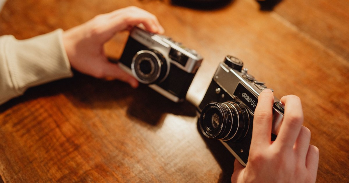 Two vintage cameras being held on a wooden table, perfect for photography enthusiasts.
