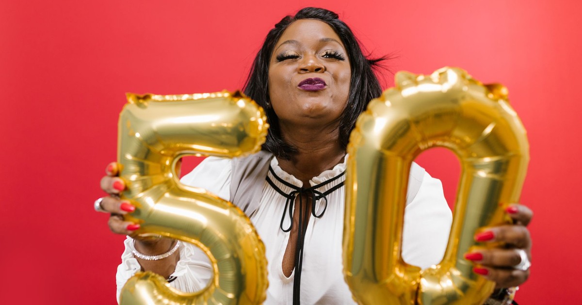 Joyful woman holding golden 50 balloons against a vibrant red background.