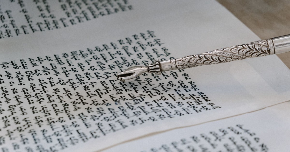 A detailed view of a silver yad pointing to Hebrew text in a Torah scroll.
