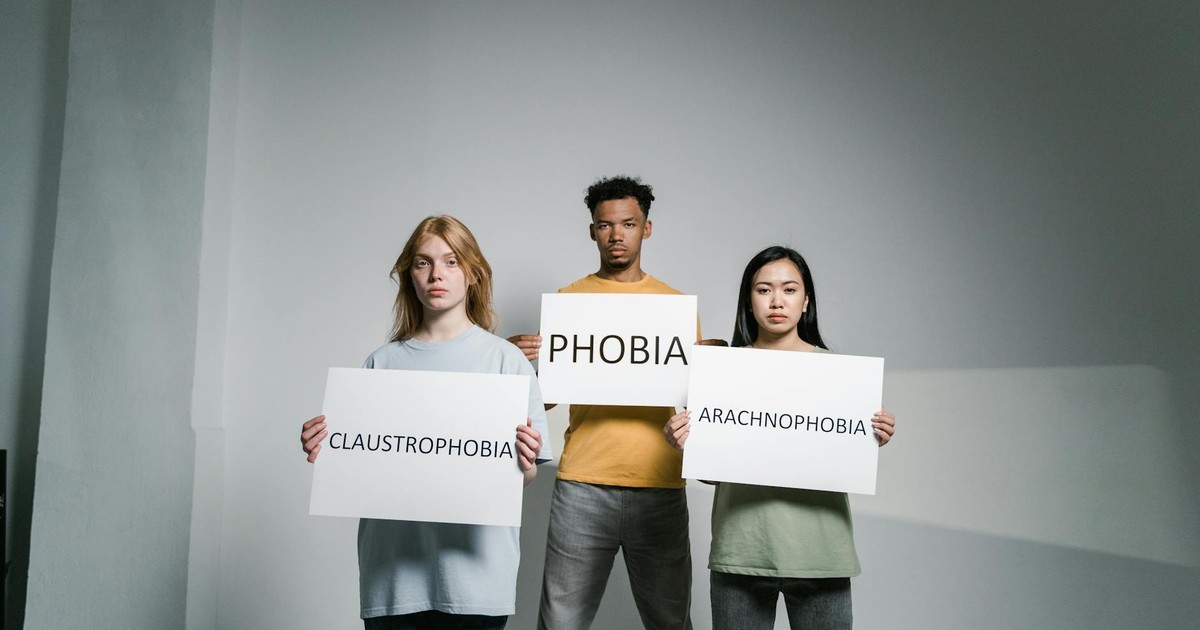 Three individuals holding signs representing various phobias, raising awareness.