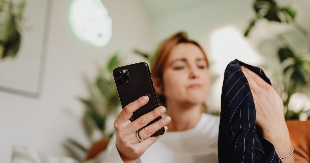 A woman uses her smartphone indoors for online shopping, holding fabric.