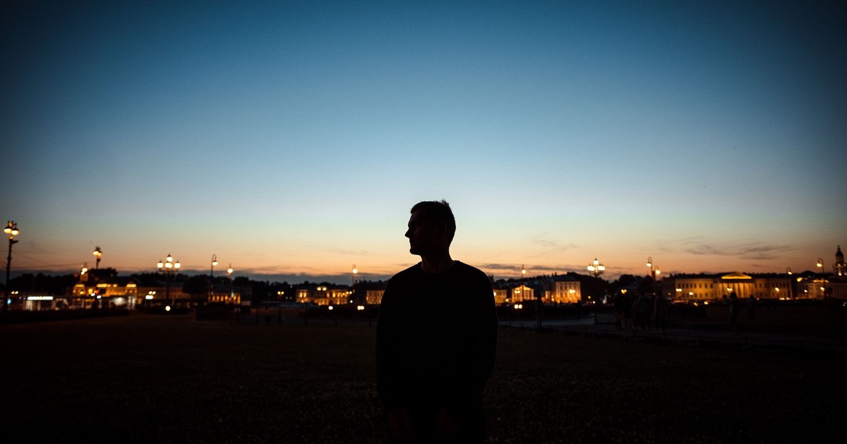 Silhouette of a man standing against a vibrant, lit city skyline at dusk.