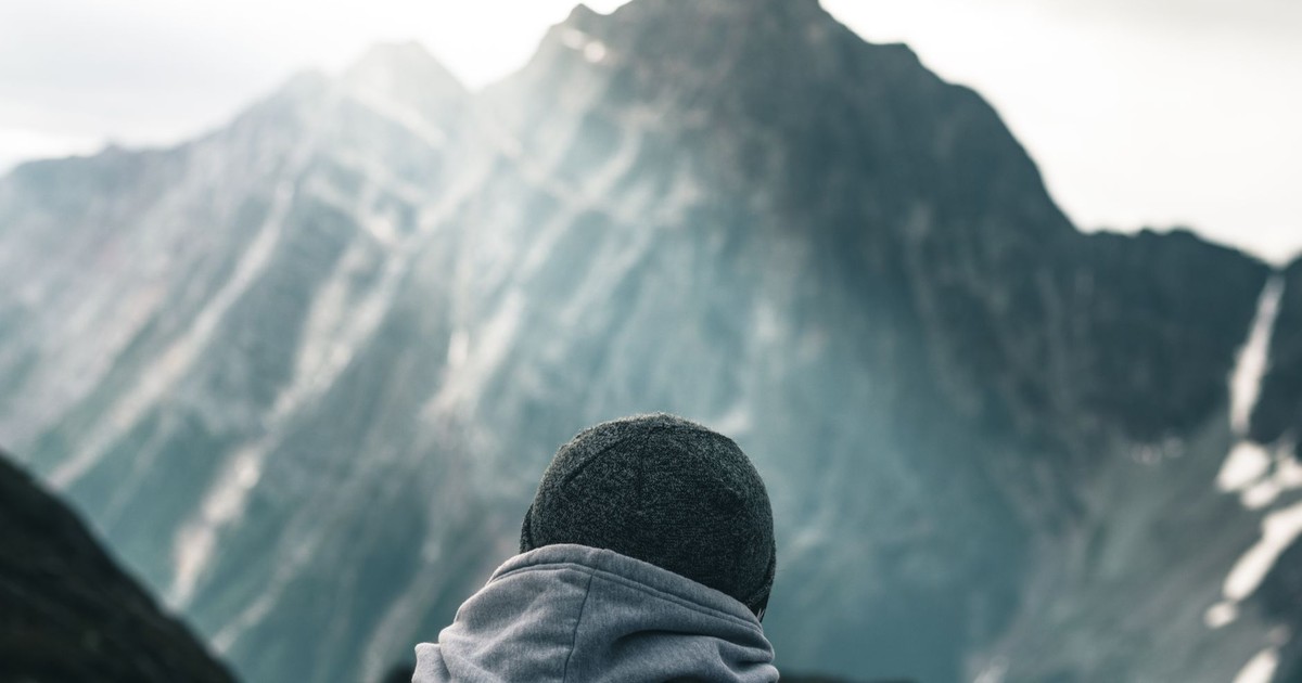 A lone adventurer gazes at a snow-capped mountain peak in winter, bathed in sunlight.