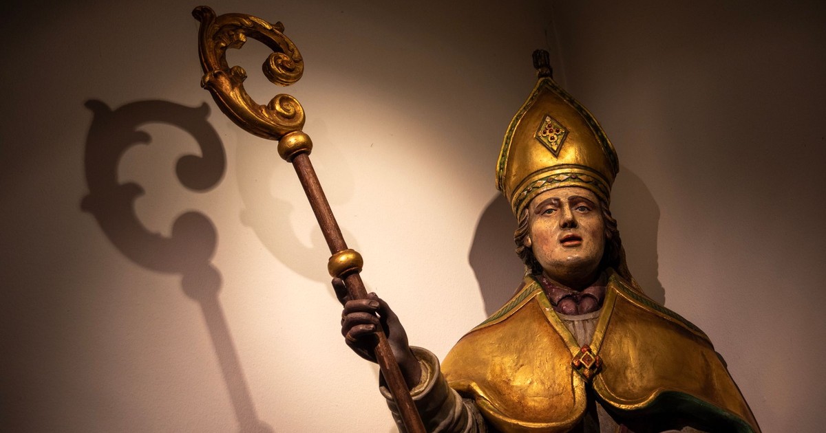 Illuminated statue of a bishop with a shadow cast on the wall in Holset, Limburg.