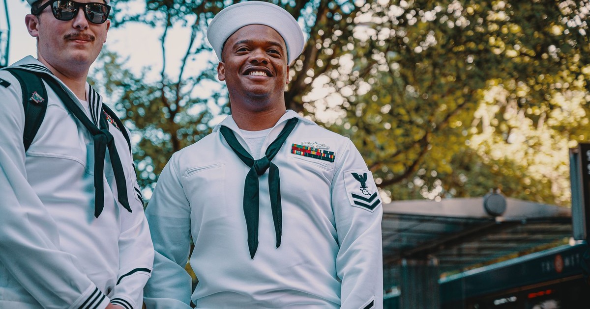 Two navy sailors in uniform smiling outdoors, capturing camaraderie and pride.