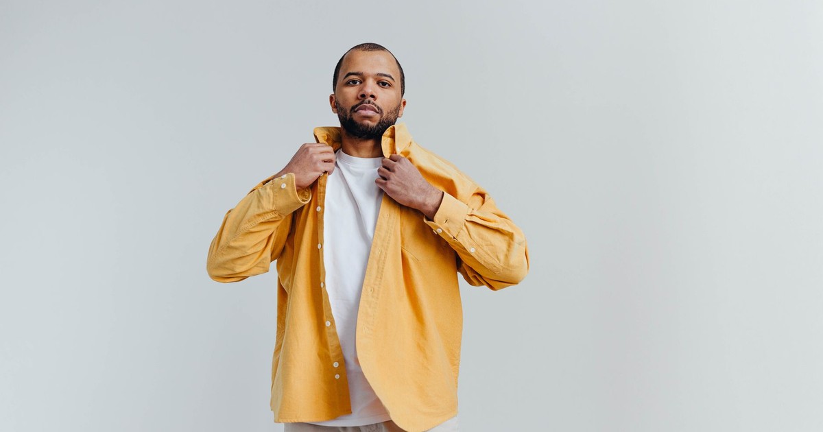 Portrait of a confident man adjusting his yellow shirt against a white background, exuding style and poise.