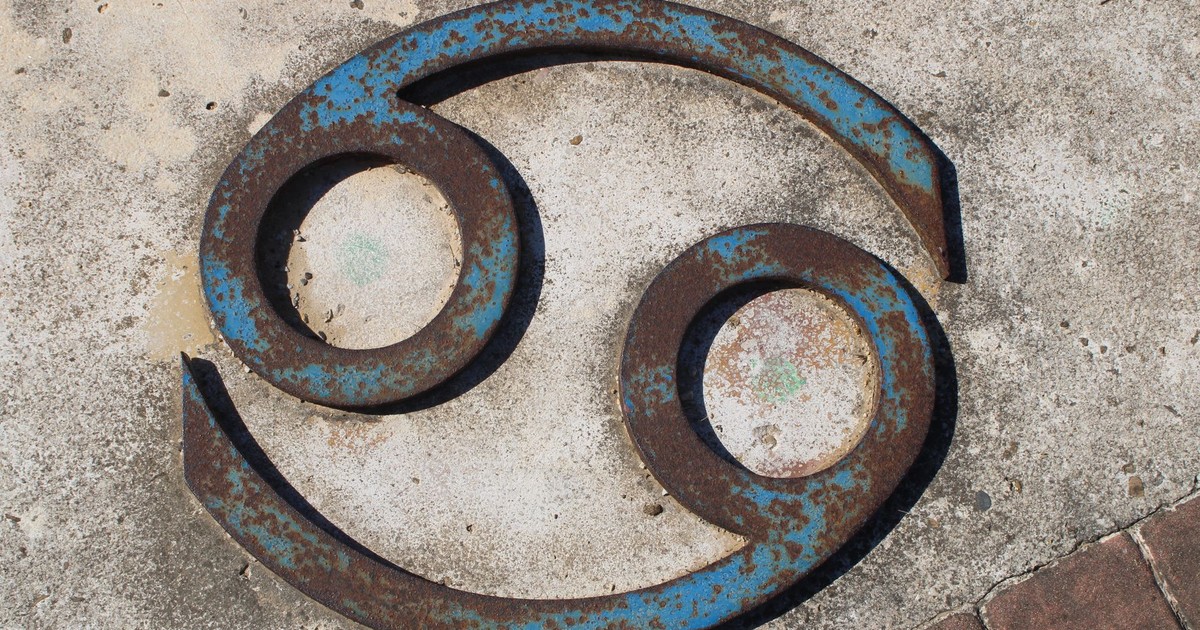 Close-up of a rusted Cancer zodiac symbol on a concrete wall.